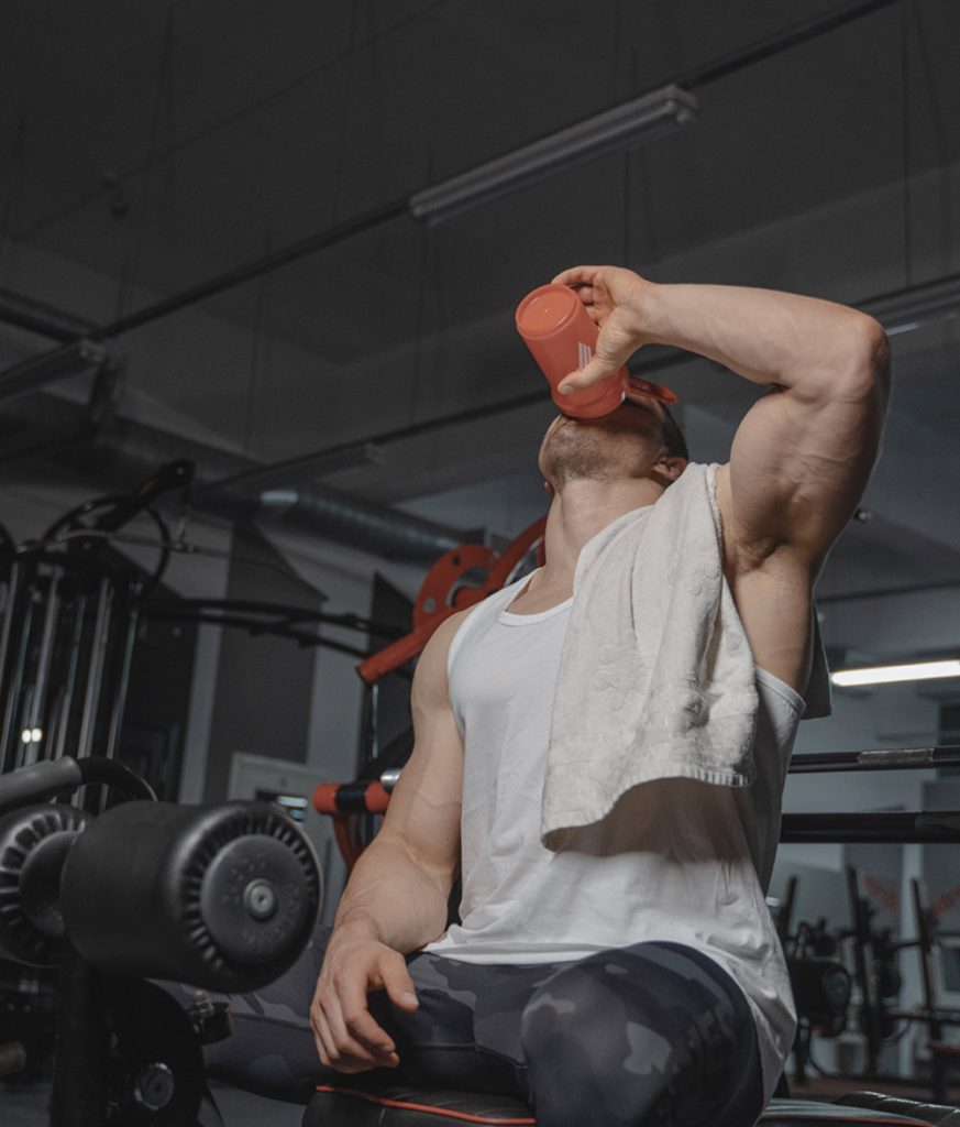 Un homme au gym avec un serviette sur son bras qui boit d'une bouteille de sport